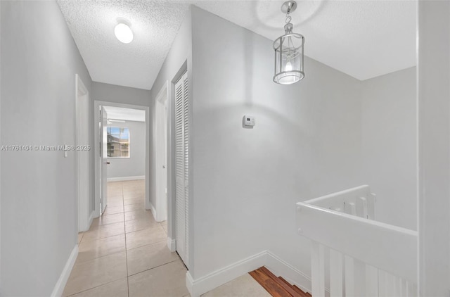 corridor with light tile patterned floors, a textured ceiling, and baseboards