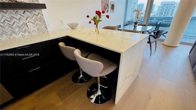 kitchen with dark cabinetry, light stone counters, a breakfast bar, light wood-style floors, and a city view