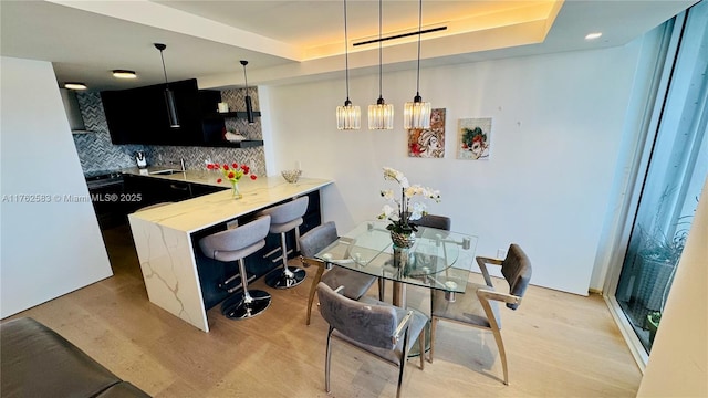 kitchen featuring decorative light fixtures, a tray ceiling, a sink, tasteful backsplash, and a breakfast bar area