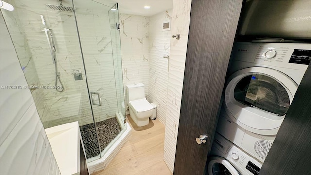 bathroom with toilet, stacked washing maching and dryer, a marble finish shower, tile walls, and tile patterned flooring