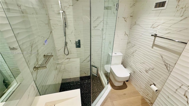 bathroom with a marble finish shower, tile walls, toilet, and visible vents