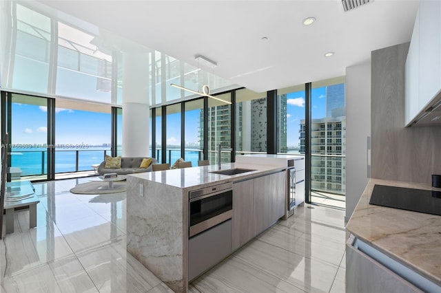 kitchen featuring a wall of windows, stainless steel microwave, modern cabinets, and a kitchen island with sink