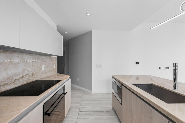 kitchen featuring a sink, modern cabinets, light stone counters, and black appliances