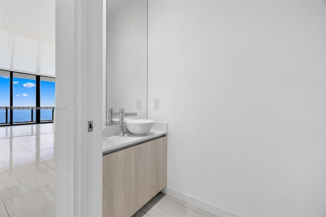 bathroom featuring baseboards, a water view, floor to ceiling windows, marble finish floor, and vanity