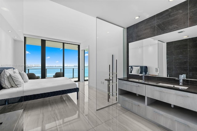 bedroom featuring access to exterior, floor to ceiling windows, a water view, and a sink