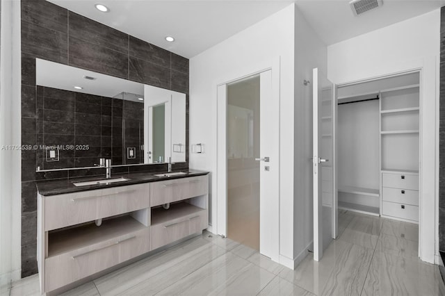 bathroom with a spacious closet, visible vents, double vanity, and a sink