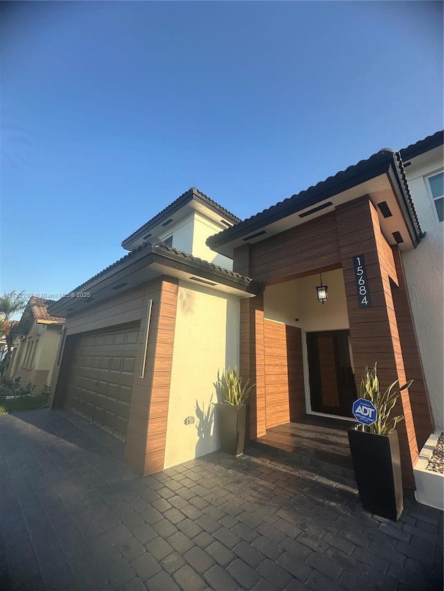 view of side of property with a tiled roof, stucco siding, driveway, and a garage