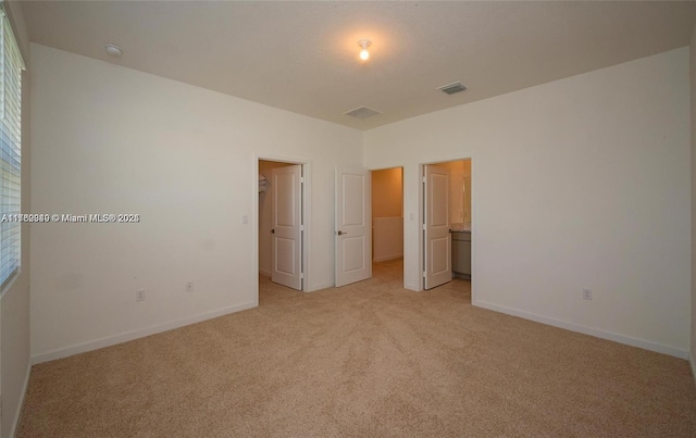 unfurnished bedroom featuring light carpet, visible vents, a walk in closet, and baseboards