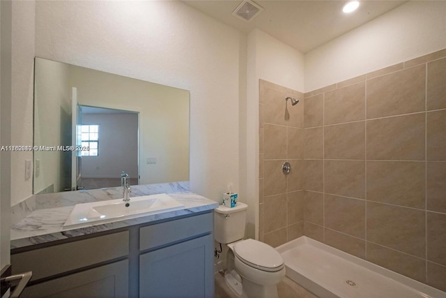 bathroom featuring vanity, toilet, visible vents, and tiled shower