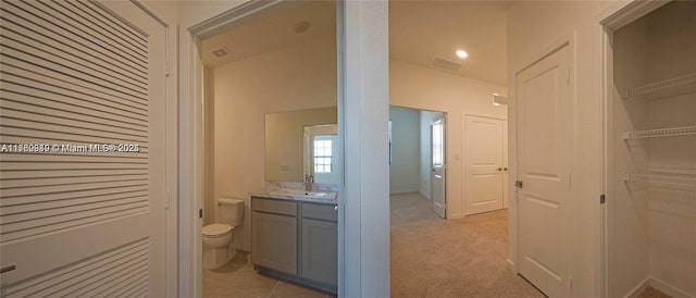 bathroom featuring vanity, a walk in closet, toilet, and visible vents