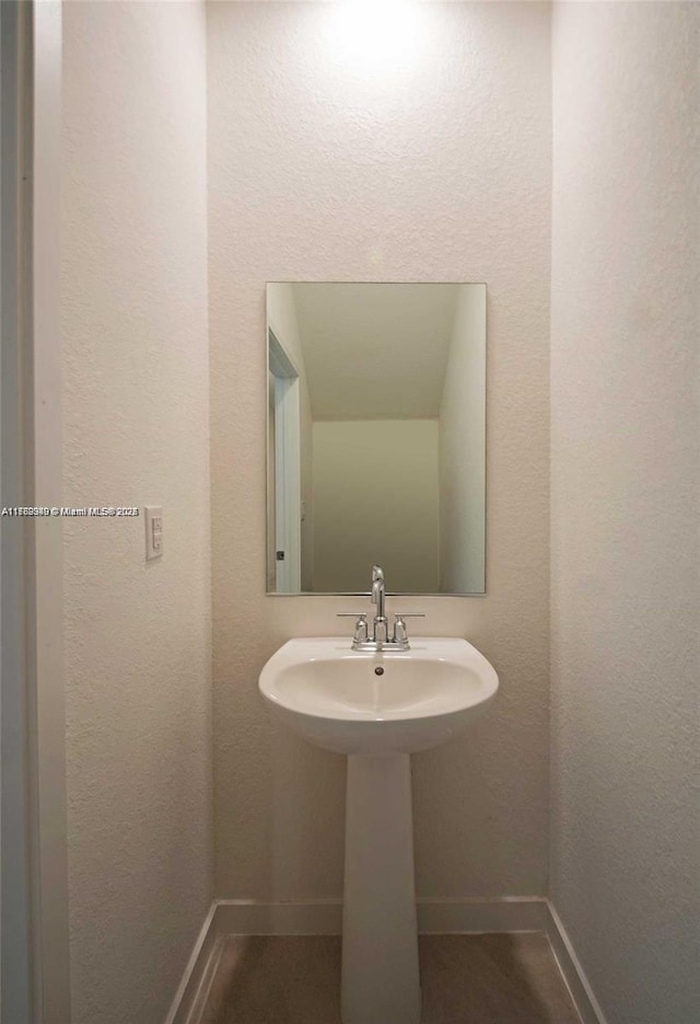 bathroom featuring a textured wall, baseboards, and a sink