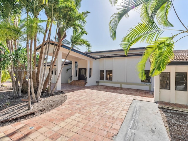 back of house with stucco siding and a tiled roof