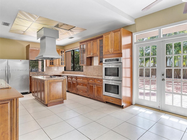 kitchen featuring visible vents, brown cabinets, island exhaust hood, tasteful backsplash, and appliances with stainless steel finishes