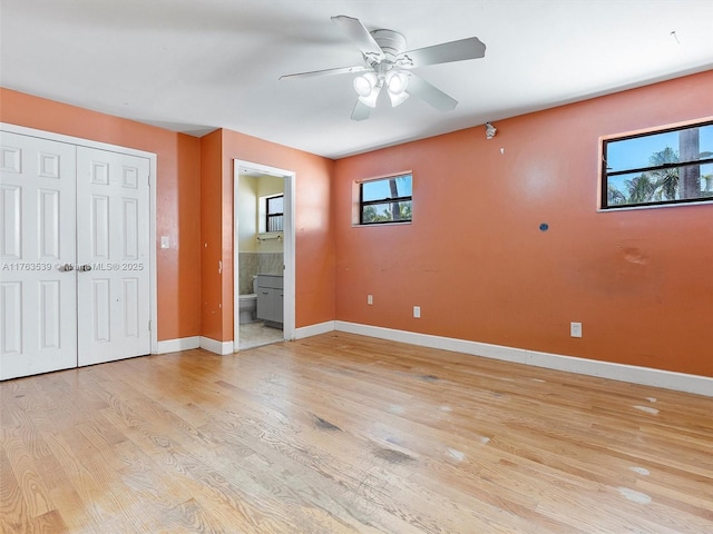 unfurnished bedroom featuring ceiling fan, baseboards, light wood-type flooring, ensuite bathroom, and a closet