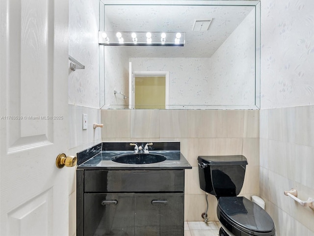 bathroom with vanity, tile walls, toilet, and wallpapered walls