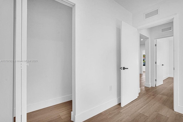 hall featuring visible vents, baseboards, and wood finished floors