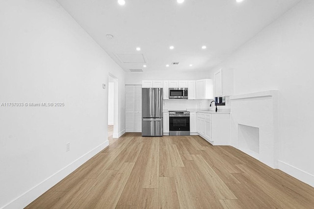 kitchen featuring a sink, white cabinets, light wood finished floors, and stainless steel appliances