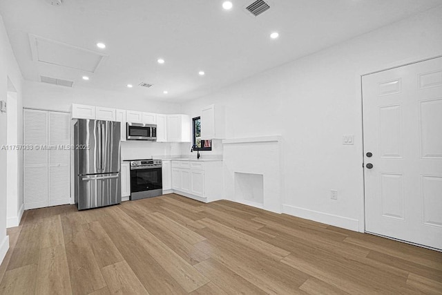 kitchen featuring visible vents, a sink, stainless steel appliances, white cabinets, and light wood-style floors