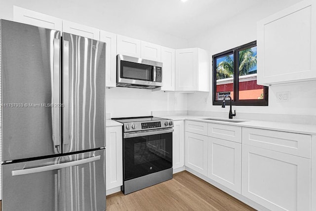 kitchen featuring light wood-type flooring, a sink, appliances with stainless steel finishes, white cabinets, and light countertops