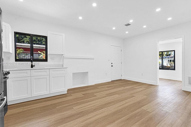 unfurnished living room featuring visible vents, baseboards, recessed lighting, light wood-style flooring, and a sink