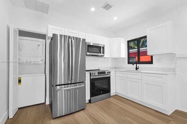 kitchen with visible vents, stacked washer / drying machine, appliances with stainless steel finishes, and a sink