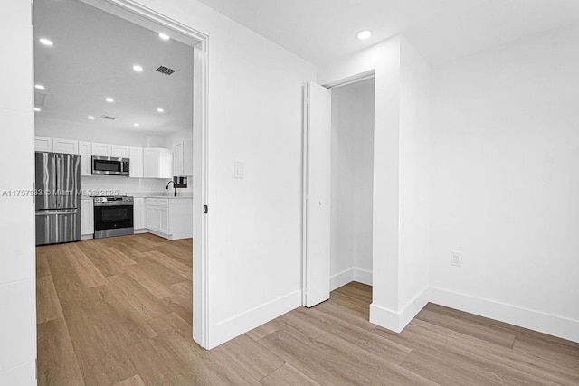 corridor with visible vents, light wood-style floors, baseboards, and a sink