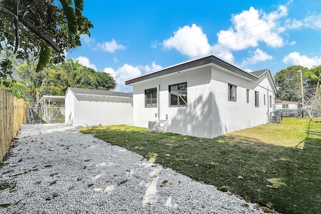 view of side of property featuring stucco siding, a yard, and fence