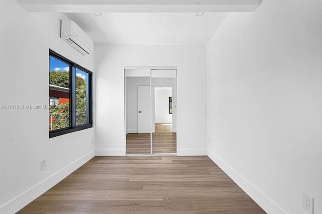 empty room with baseboards, a wall unit AC, and wood finished floors