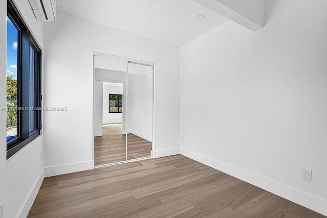 spare room featuring a wall mounted air conditioner, baseboards, and wood finished floors