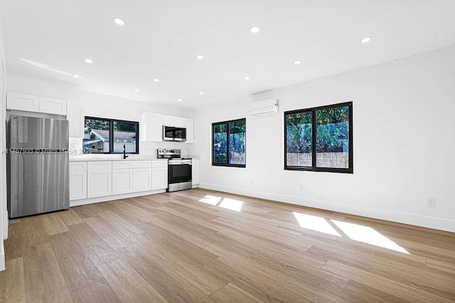 unfurnished living room featuring recessed lighting, baseboards, light wood finished floors, and a wall mounted AC