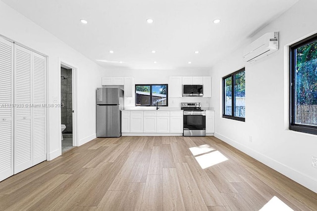 kitchen with baseboards, light wood finished floors, stainless steel appliances, an AC wall unit, and white cabinetry