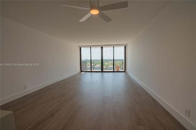 spare room featuring ceiling fan, dark wood-type flooring, a wall of windows, and baseboards