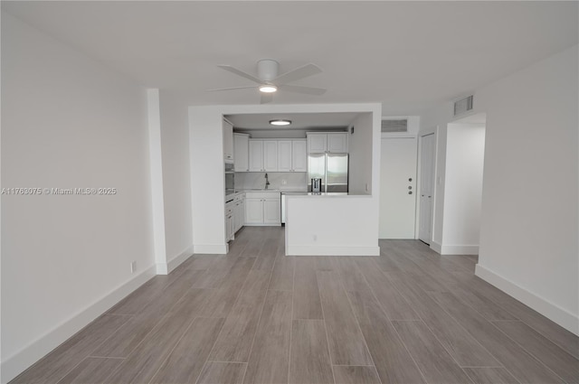 unfurnished living room featuring wood finish floors, visible vents, baseboards, and ceiling fan