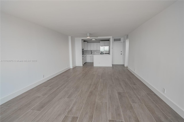 unfurnished living room with wood finish floors, visible vents, baseboards, and a ceiling fan