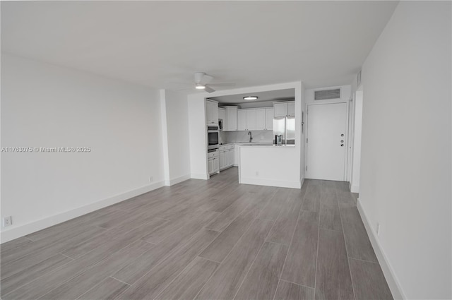 unfurnished living room with visible vents, wood finish floors, baseboards, and ceiling fan