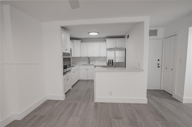 kitchen with wood finish floors, visible vents, a sink, stainless steel appliances, and white cabinets