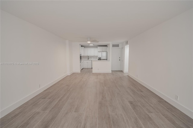 unfurnished living room featuring visible vents, light wood-type flooring, and baseboards