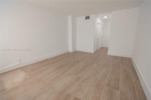 empty room featuring light wood-style flooring, visible vents, and baseboards