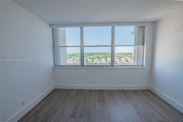 empty room featuring baseboards, dark wood-type flooring, and a healthy amount of sunlight