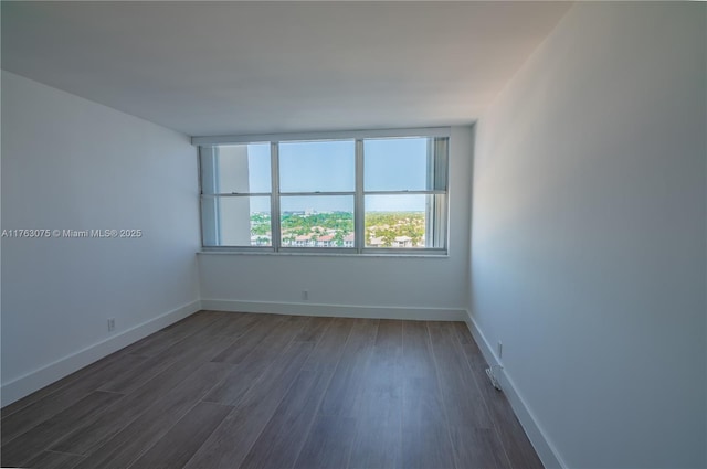 spare room featuring baseboards and dark wood-style floors