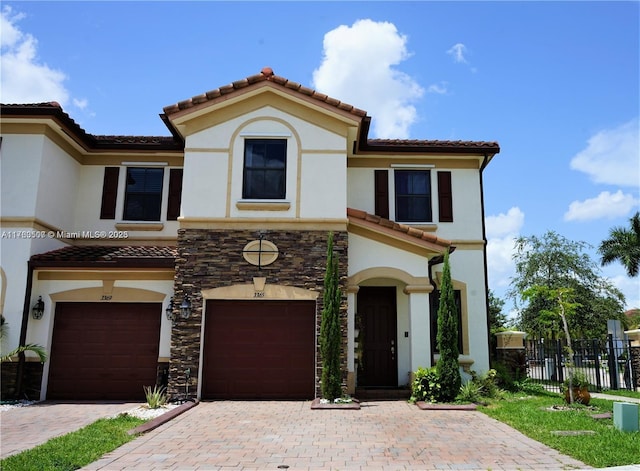 mediterranean / spanish-style home featuring fence, a tile roof, stucco siding, decorative driveway, and a garage