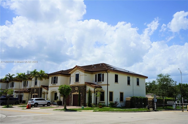 view of front of home featuring a tiled roof, fence, roof mounted solar panels, and stucco siding