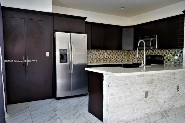 kitchen with a peninsula, light countertops, marble finish floor, appliances with stainless steel finishes, and tasteful backsplash