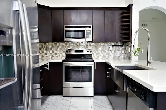 kitchen with light countertops, a peninsula, marble finish floor, and appliances with stainless steel finishes