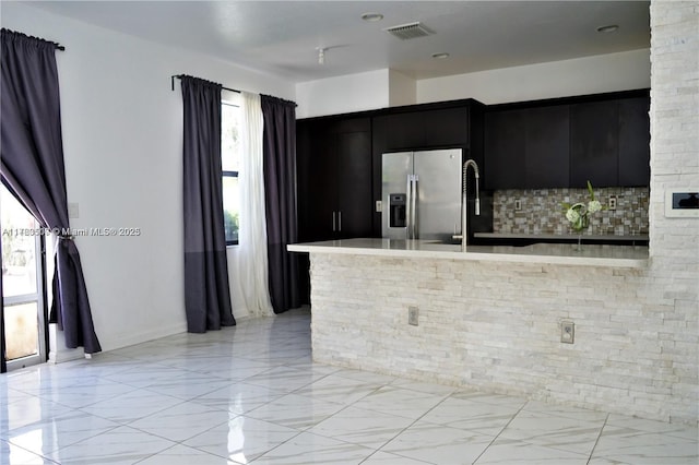 kitchen featuring visible vents, stainless steel refrigerator with ice dispenser, backsplash, dark cabinetry, and light countertops