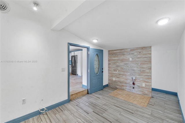 spare room with baseboards, visible vents, lofted ceiling with beams, wood walls, and an accent wall