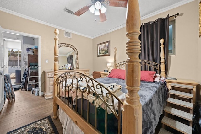 bedroom with visible vents, ornamental molding, a textured ceiling, and wood finished floors