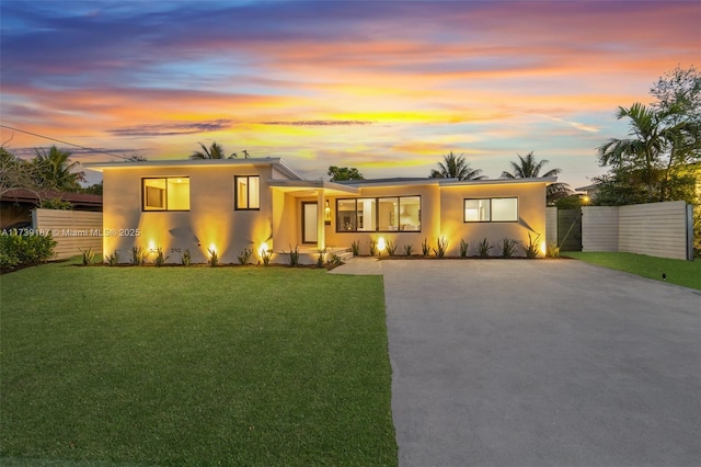 view of front facade featuring stucco siding, a lawn, concrete driveway, and fence