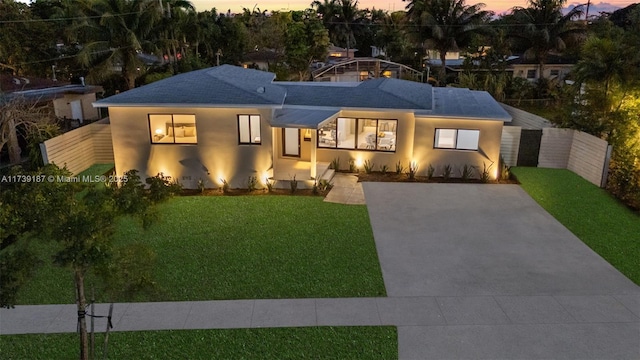 view of front facade with stucco siding, driveway, a yard, and fence