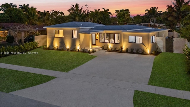 view of front facade featuring stucco siding, concrete driveway, a front lawn, and fence